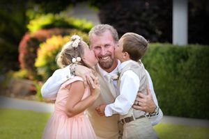 Heartwarming family embrace on lush garden lawn during wedding celebration.