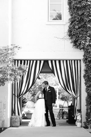 Black and white wedding photo framed by striped curtains in elegant archway.