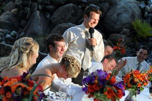Wedding party gathered around a table with vibrant floral centerpieces during an outdoor reception.