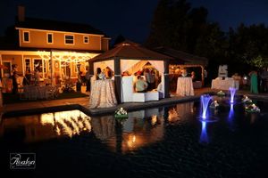 Elegant poolside wedding reception at night with illuminated fountains and house in background.