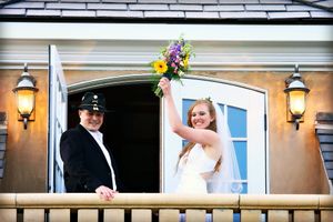 Wedding couple sharing a joyful moment on a balcony with decorative floral arrangement.