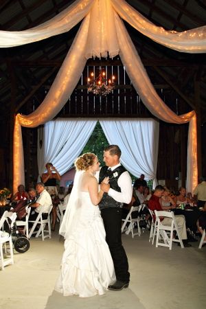 Wedding couple's first dance under draped fabric and twinkle lights in rustic barn venue.