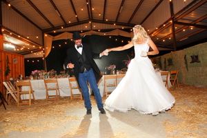 A couple dances joyfully in a rustic venue decorated with twinkling lights during their wedding reception.