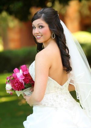 A bride in a white strapless gown holds a vibrant pink and red bouquet while posing outdoors.