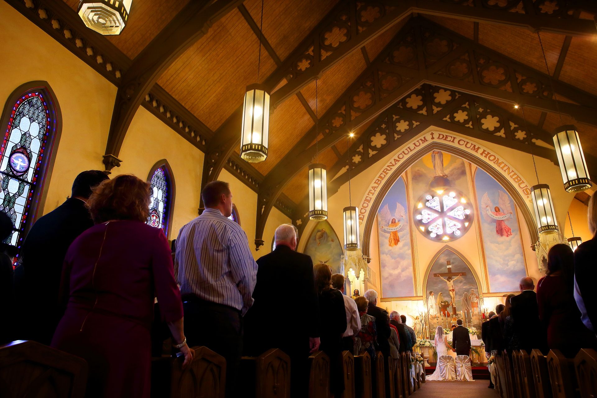 Interior of a church during a wedding ceremony with stained glass windows and vaulted ceilings.