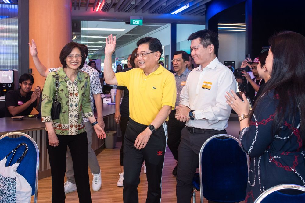 Group of professionals in colorful attire waving and smiling at a corporate bowling event venue.