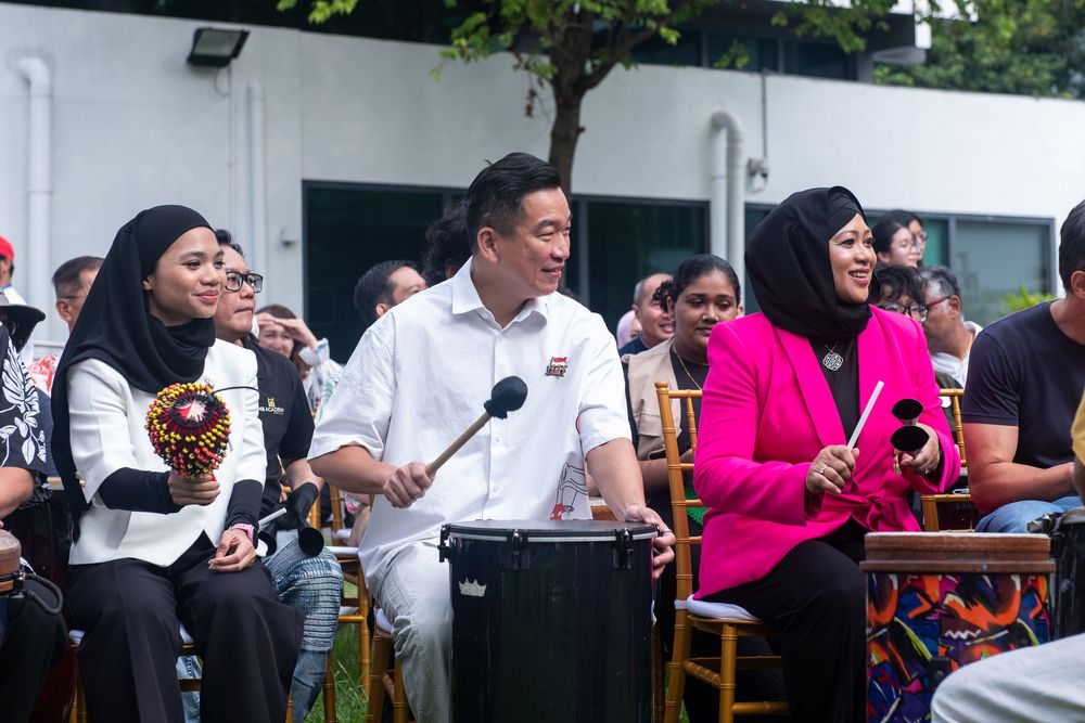 Group of people playing drums outdoors at a cultural event, wearing traditional and formal attire.