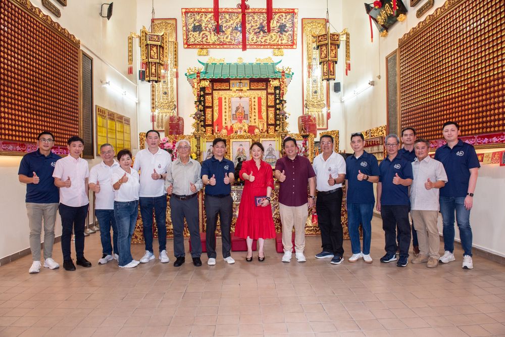 Group of people posing together inside a colorful Chinese temple with red and gold altar decorations.
