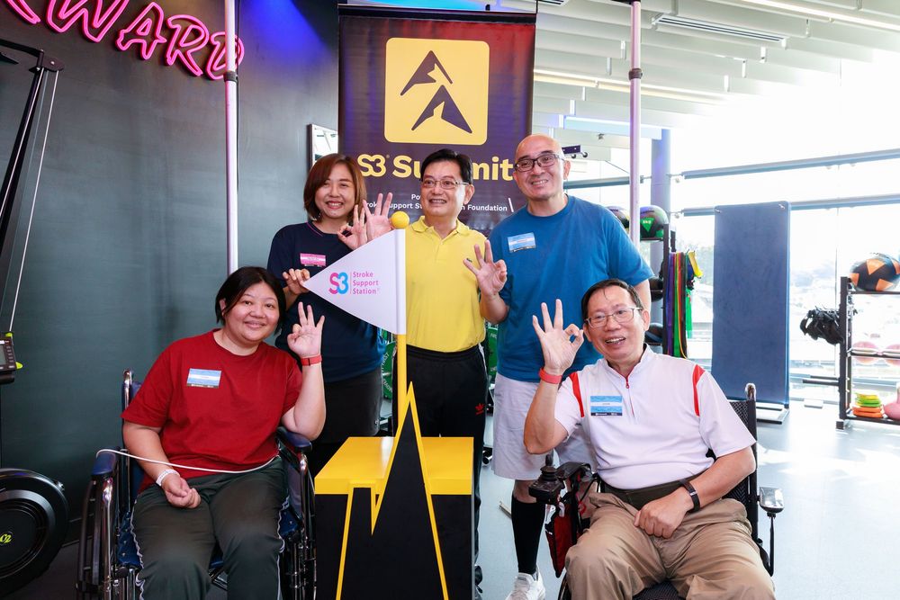 Group of five people smiling and waving at S3 Summit event, including two individuals in wheelchairs.