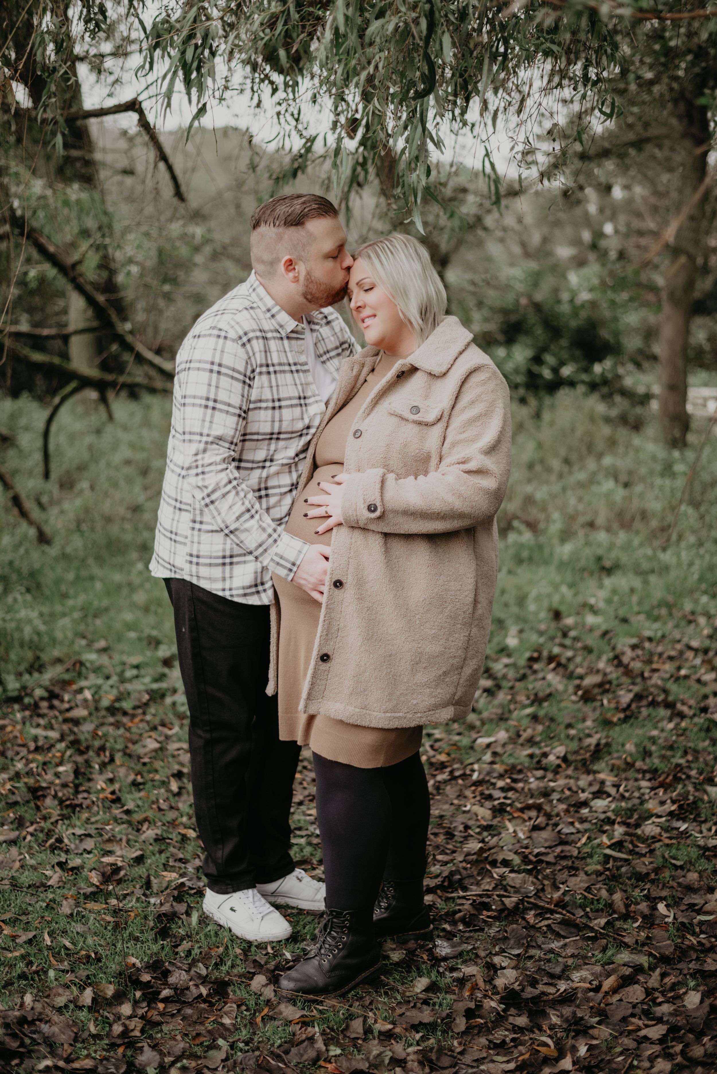 Couple embraces tenderly among fallen leaves in moody forest setting.