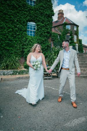 Wedding couple in formal attire walking outside an ivy-covered brick building.