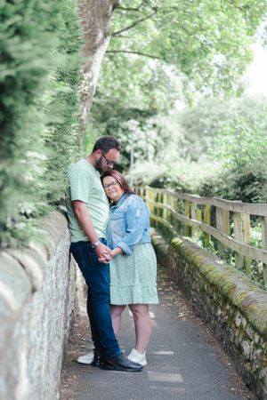 Couple shares intimate moment on stone bridge pathway surrounded by lush greenery.