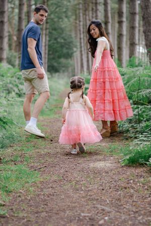 Family wearing matching pink dresses walks along forest path together.