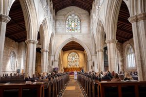 Gothic church interior with vaulted ceiling, stained glass windows, and wooden pews lined up in rows.