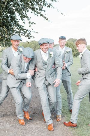 Groomsmen in matching gray suits laugh together outdoors during wedding celebration.