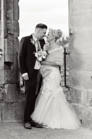 A bride and groom share an intimate moment in black and white photography against a stone archway during their wedding.