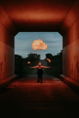 Fire performer in a tunnel with dramatic lighting and explosion effect in background.