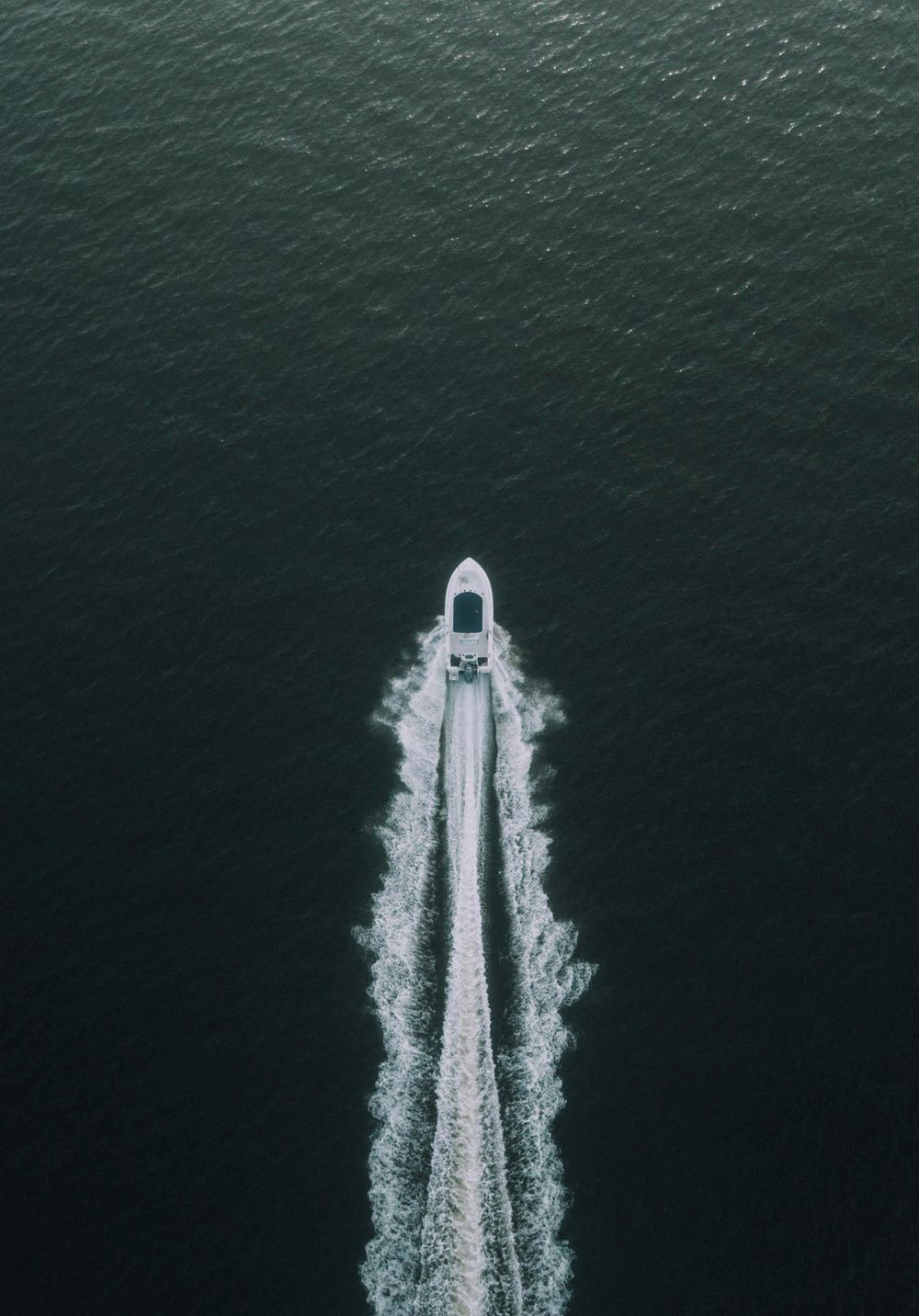 Aerial drone view of a speedboat leaving a white wake trail on dark green ocean water.
