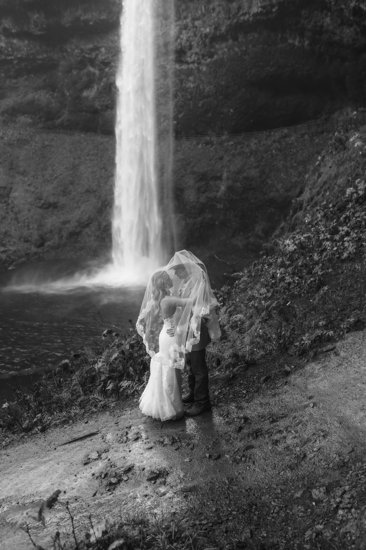 A couple shares a romantic moment on a misty beach near dramatic coastal cliffs during their wedding.