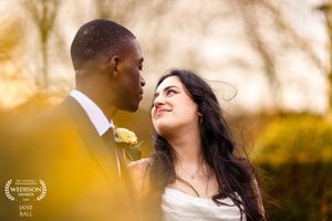 A romantic outdoor wedding photo with a couple in traditional attire smiling at each other during golden hour sunset.