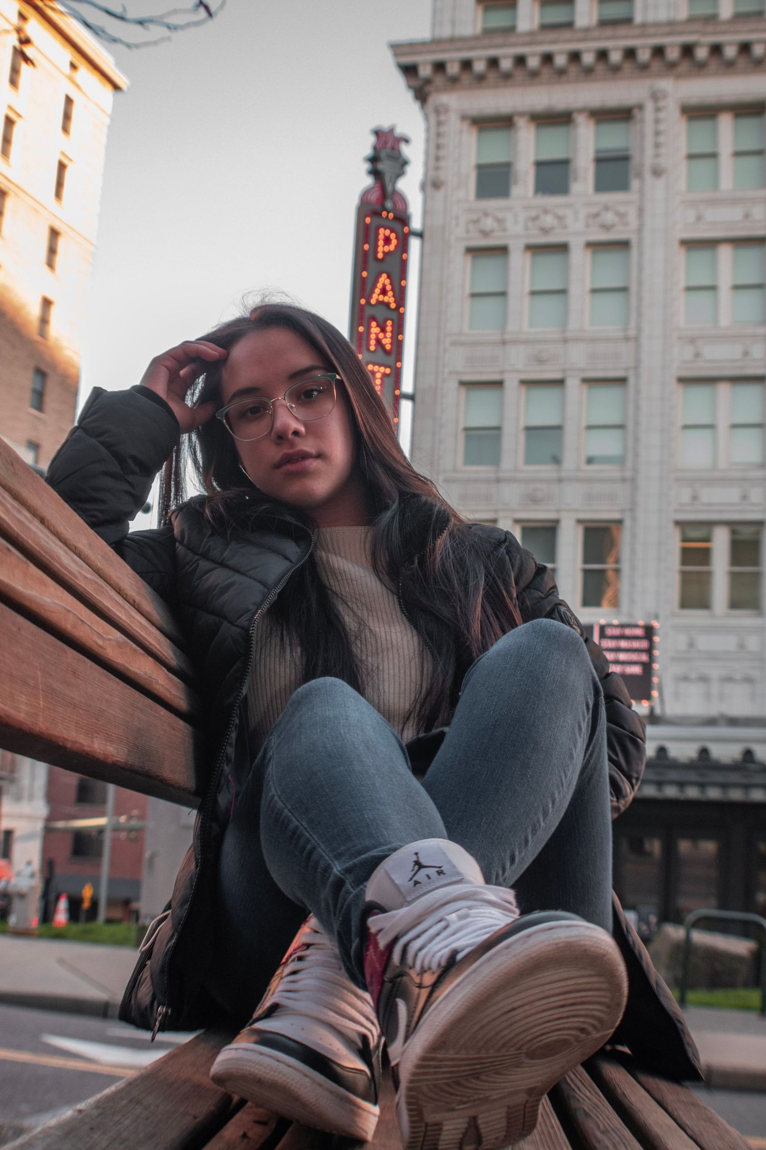 Urban portrait of person in casual wear sitting on bench with vintage theater sign in background.
