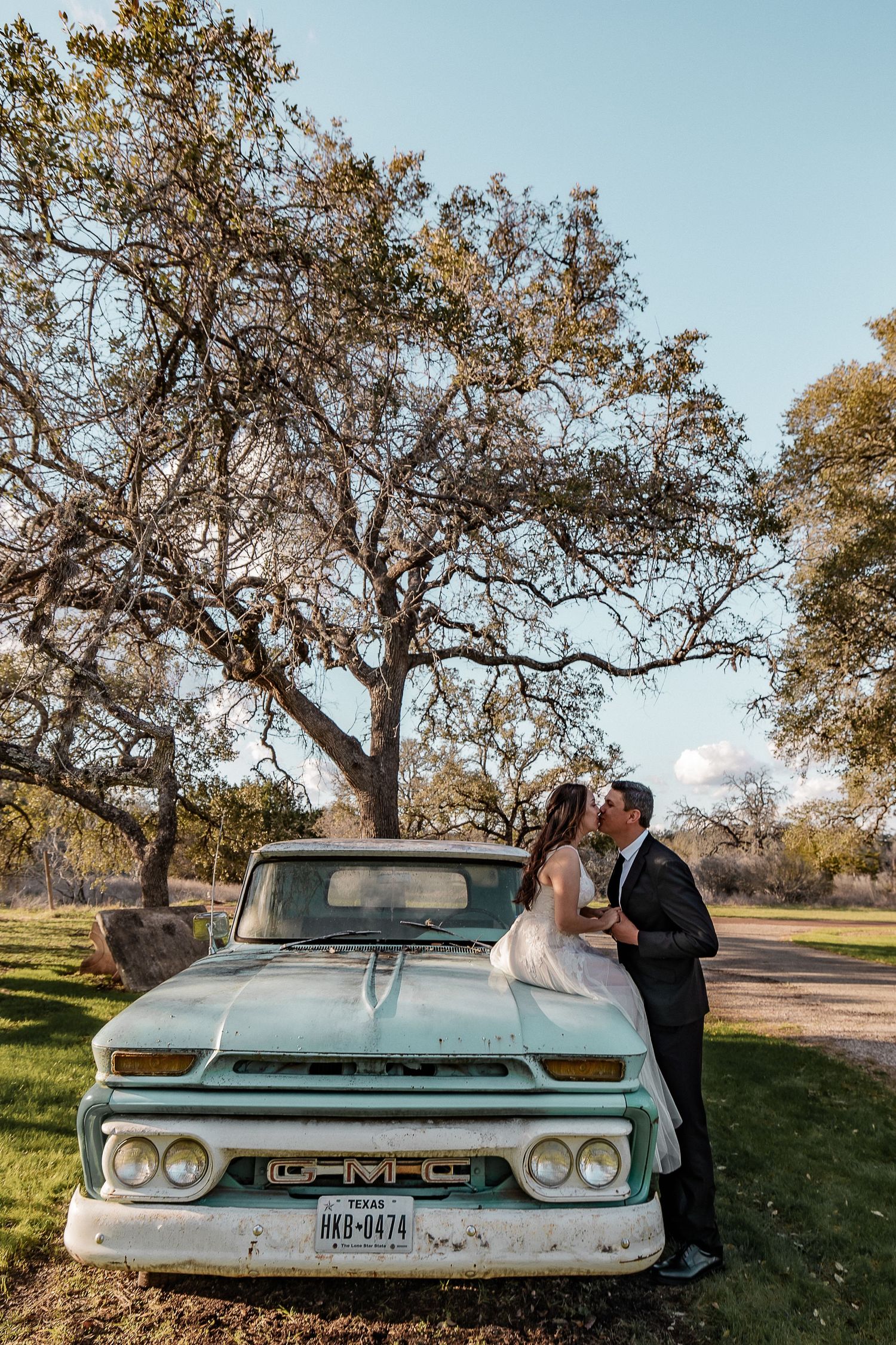 A vintage light blue car serves as a romantic backdrop for wedding photos against an autumn landscape.