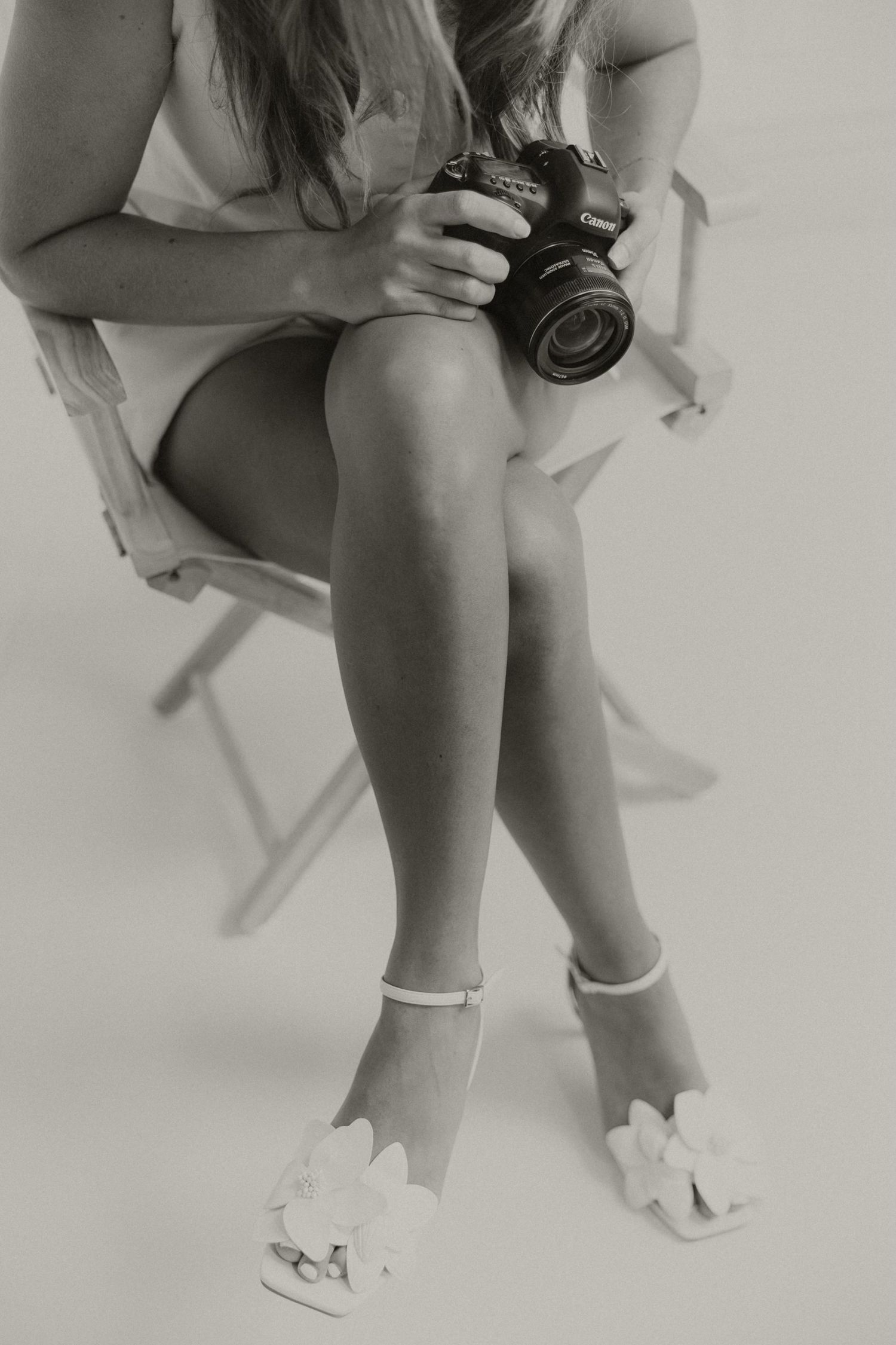 Black and white image of legs with camera and white bow shoes.