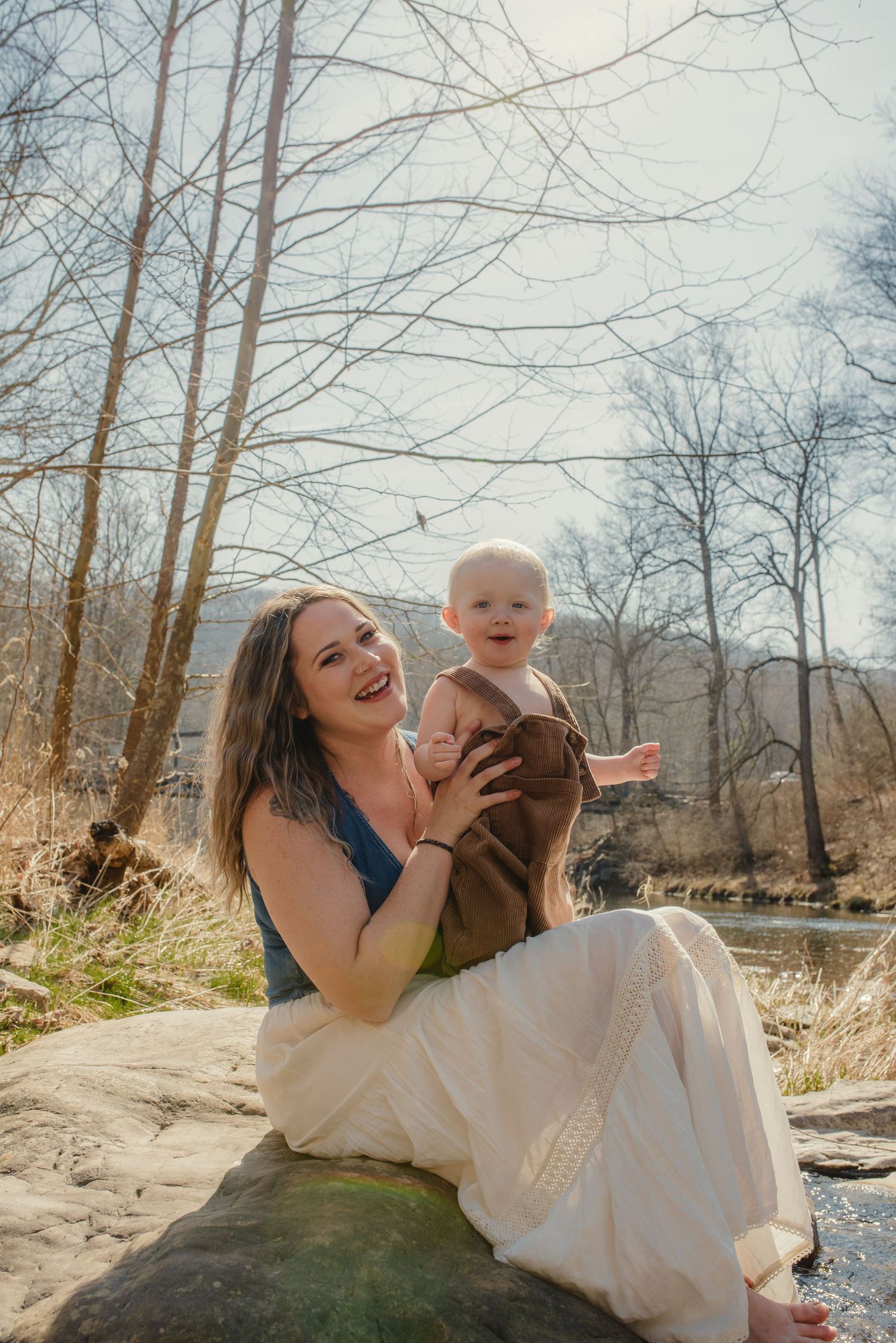 Joyful moment shared on a rock by a creek with bare winter trees in the background.