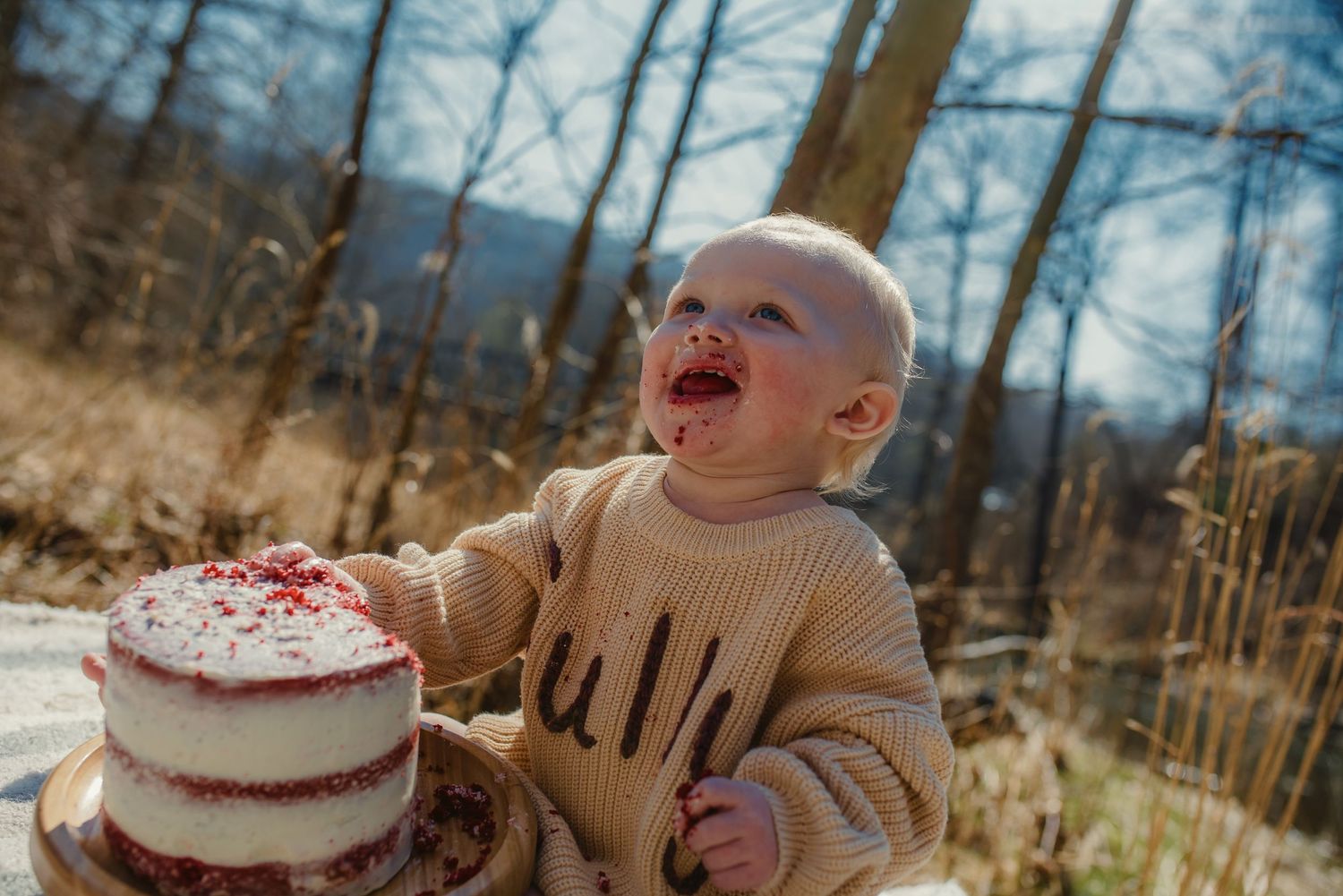 Baby's first cake smash photography session captured in natural outdoor setting with white frosted dessert.