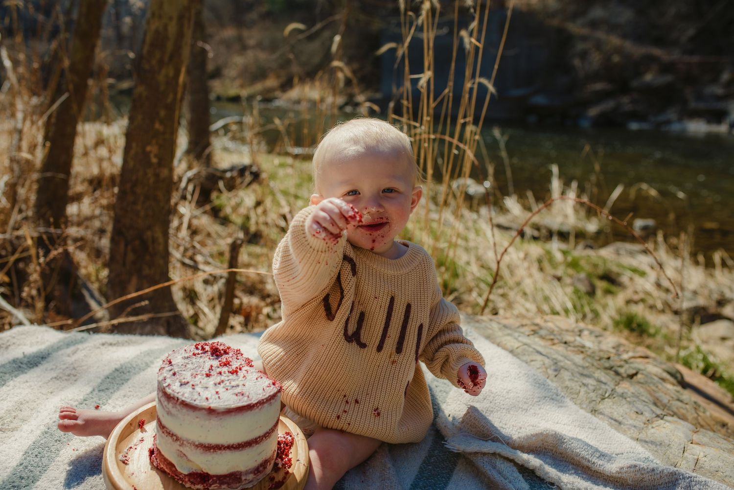 A cake smash photography session with a small child and white frosted cake in natural setting.