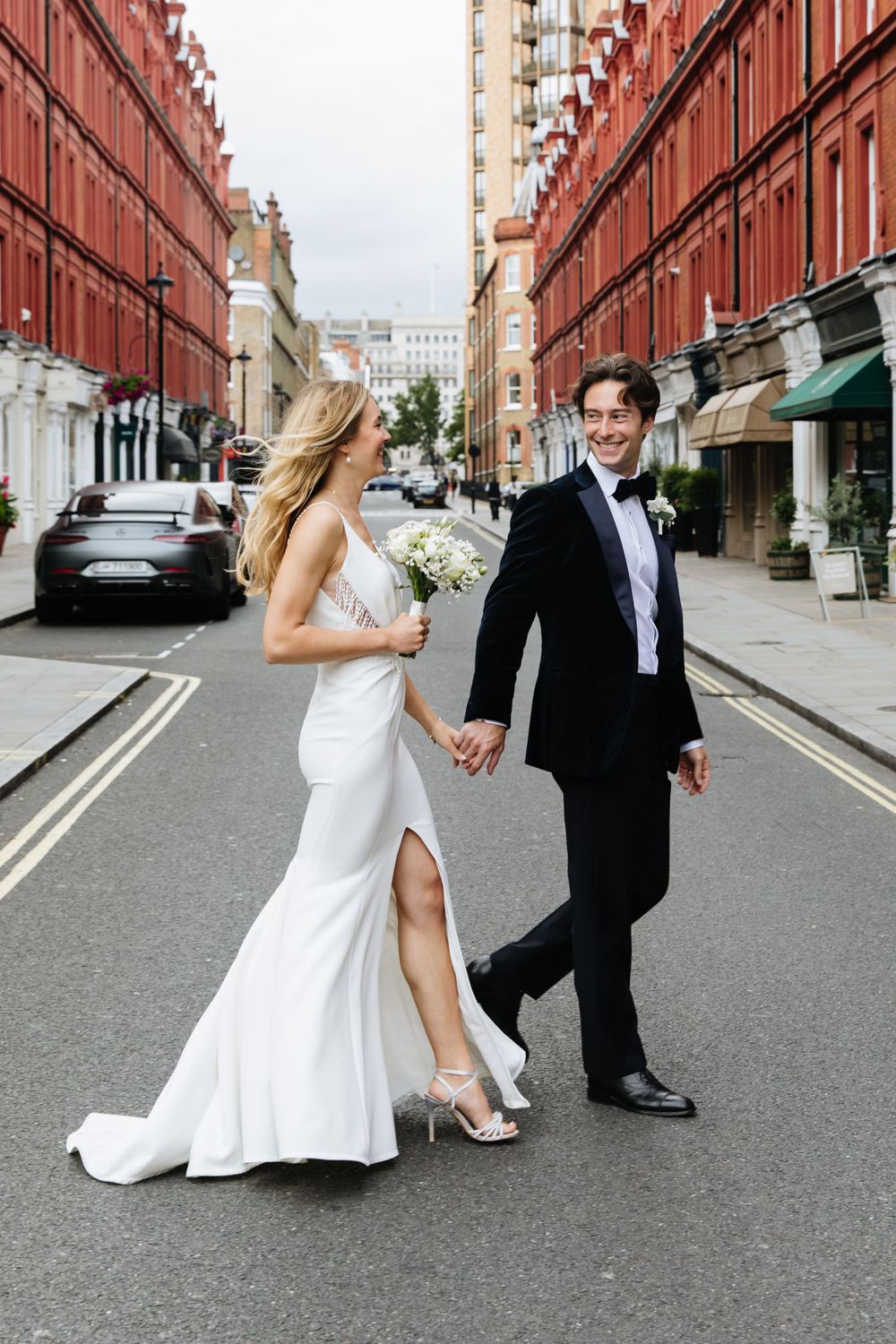 Newlyweds walking down city street with red brick buildings in London.