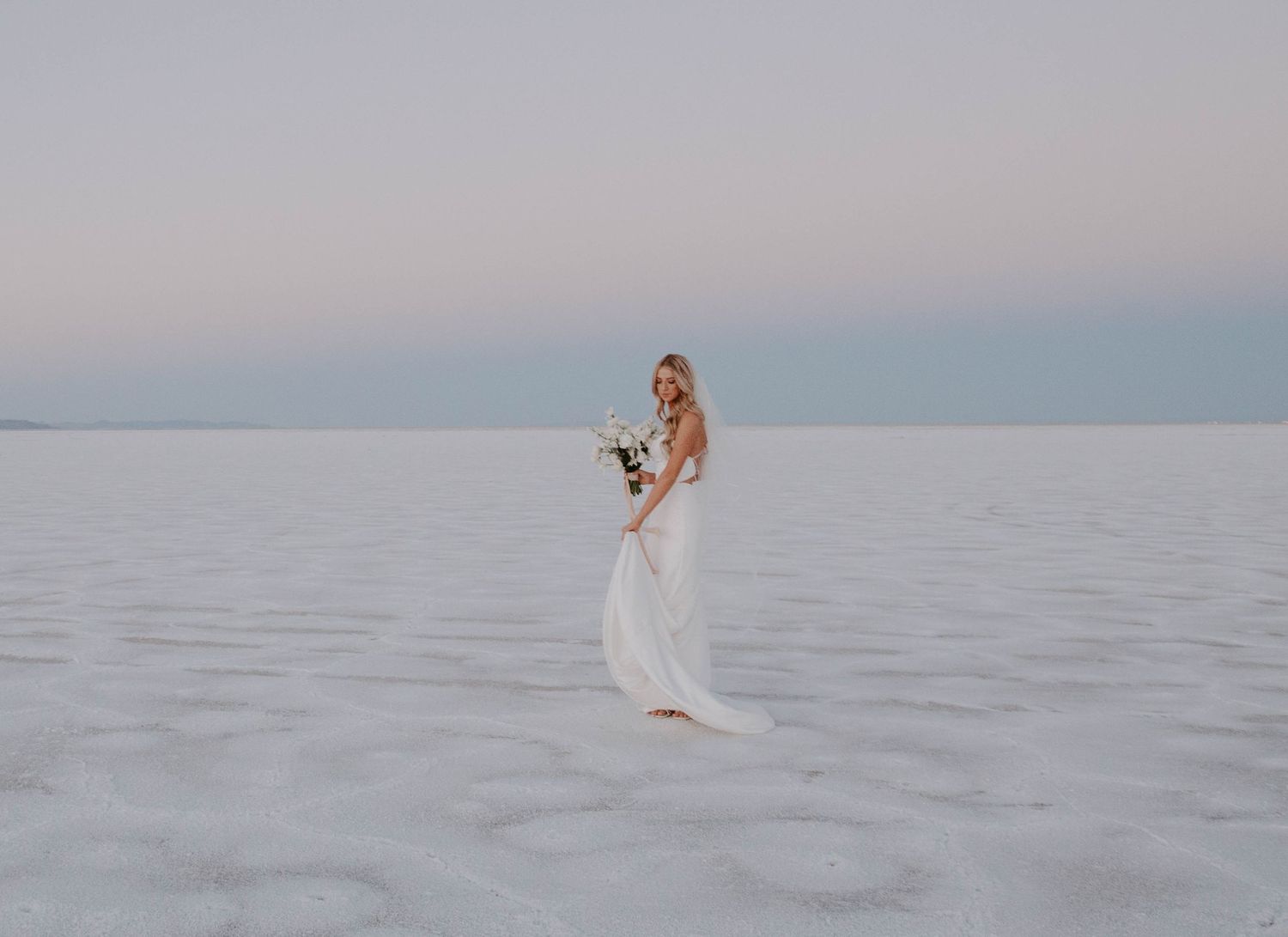 Ethereal portraits on salt flats during sunset with flowing dress in soft pastel light.