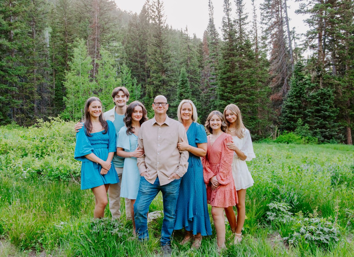 Family portrait session in a lush mountain meadow with evergreen trees.