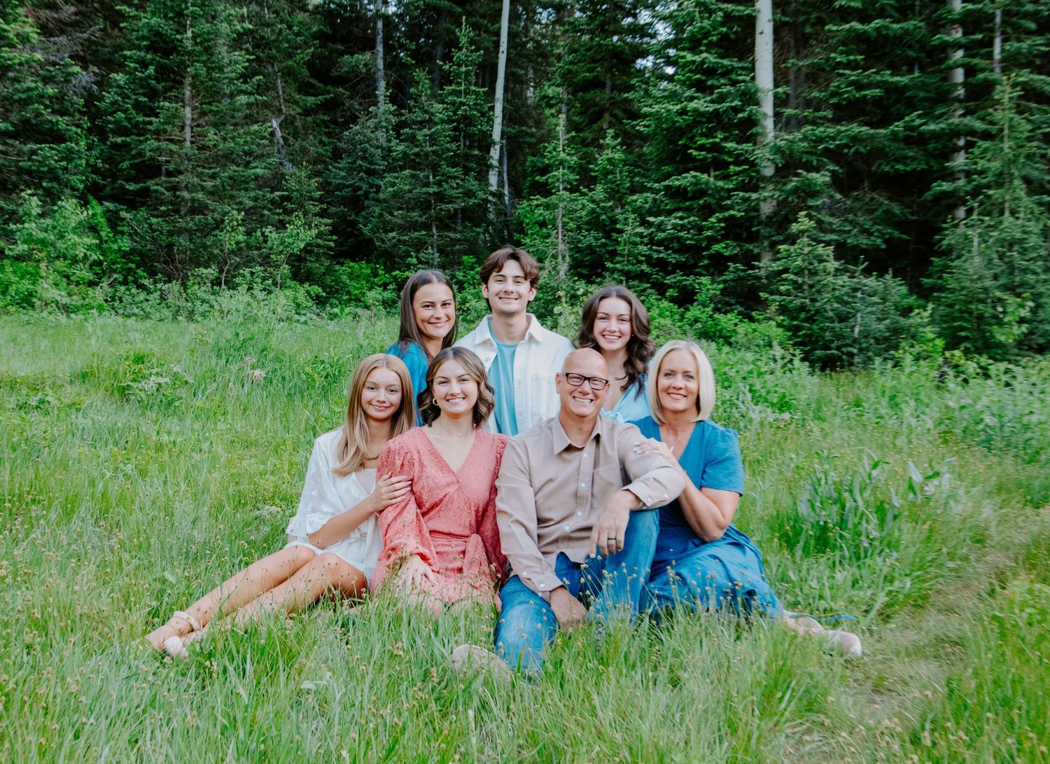 Family group sitting together on grass with evergreen forest in the background.