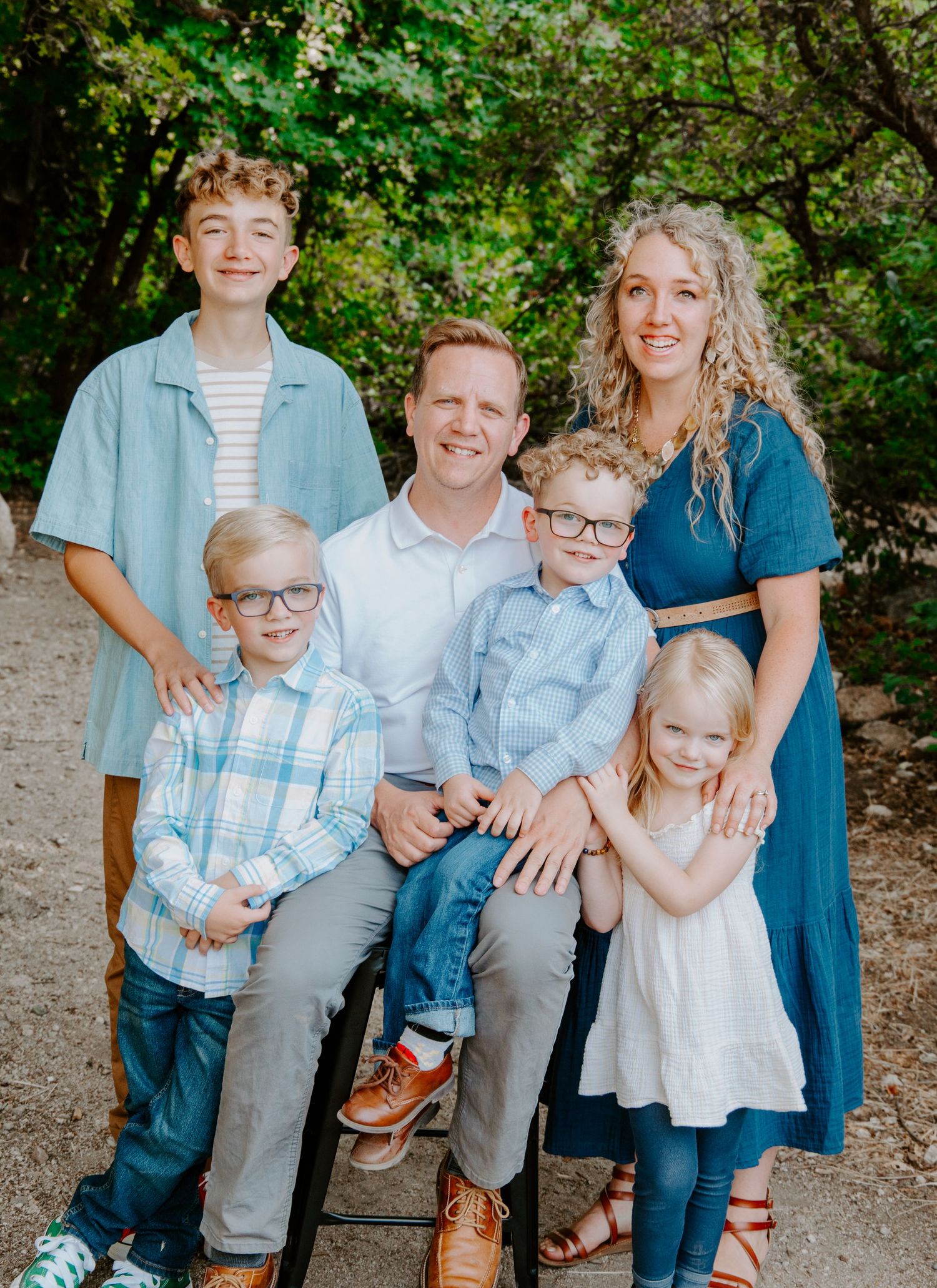 Family portrait in coordinating blue and white outfits against natural foliage background.