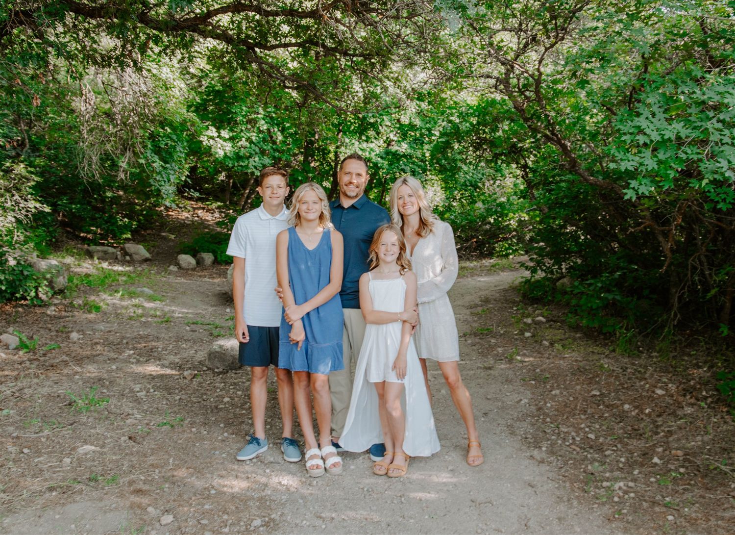 Small family group posing on dirt path surrounded by lush green foliage.