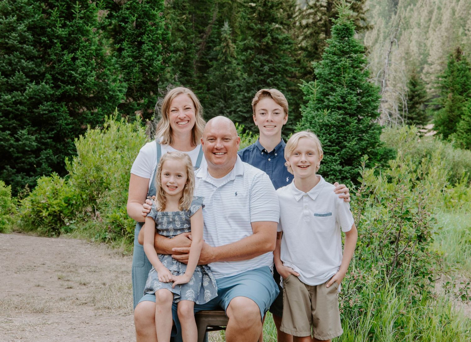 An outdoor mountain portrait with evergreen trees and rocky cliffs in the background.