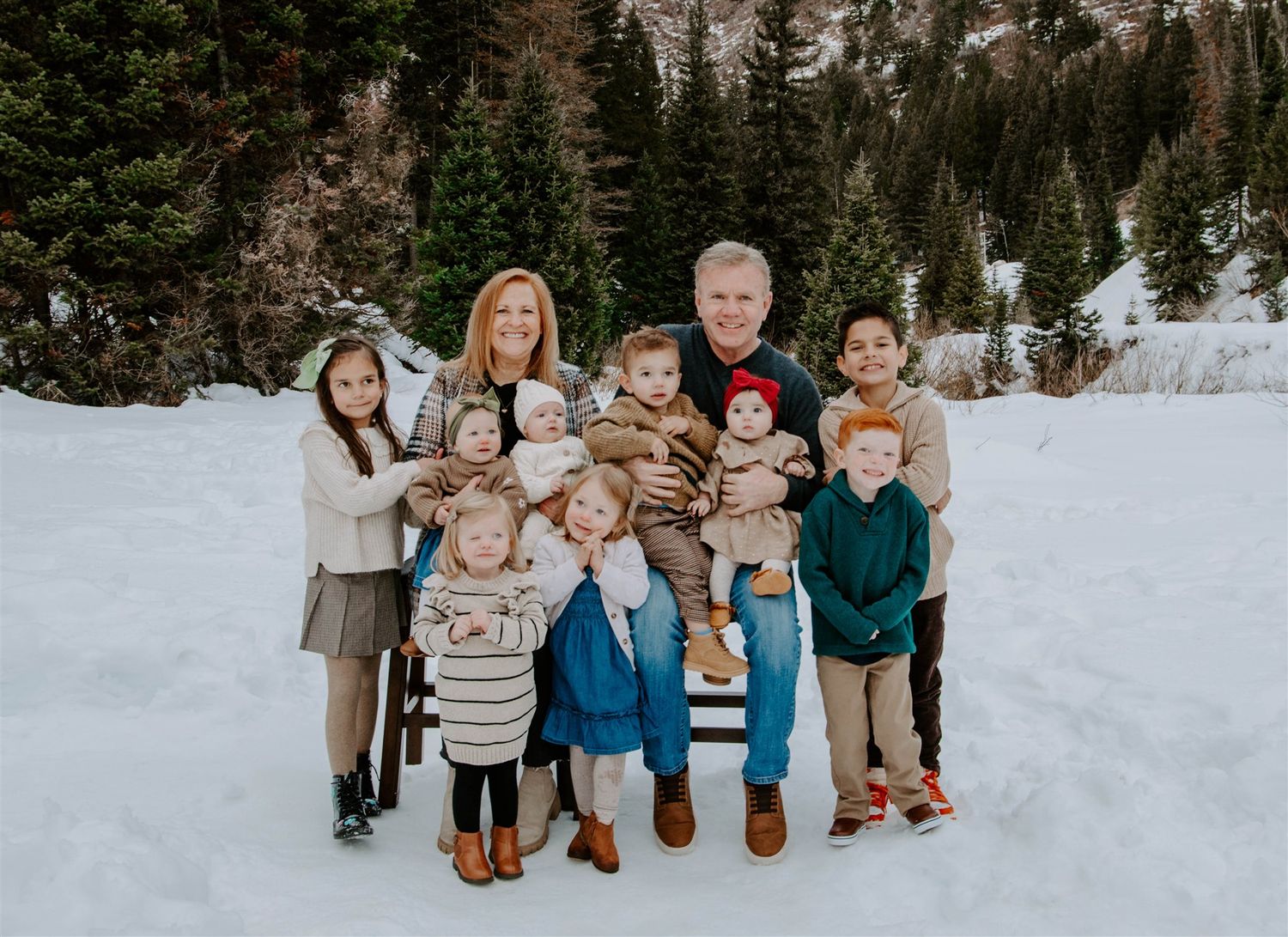 A large group portrait in a snowy mountain setting surrounded by evergreen trees.