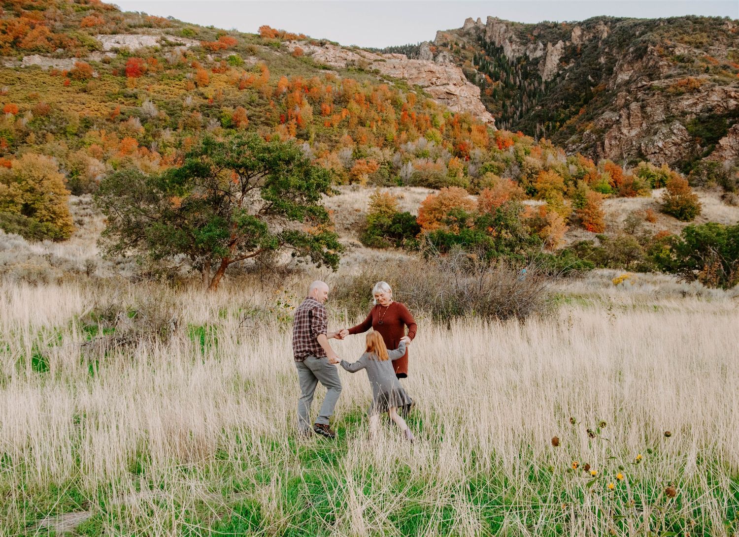 Couple walking through tall grass field with autumn colored mountains in the background.