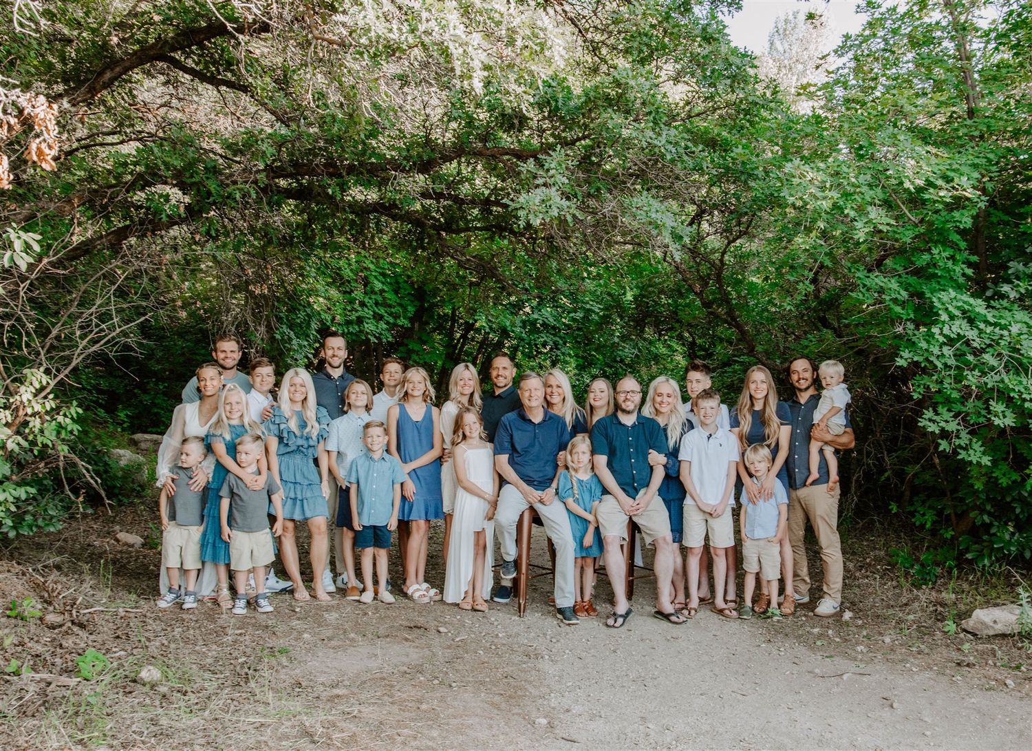 Large extended family in coordinating blue and white outfits posing together on nature path. Utah influencer Carli Williams