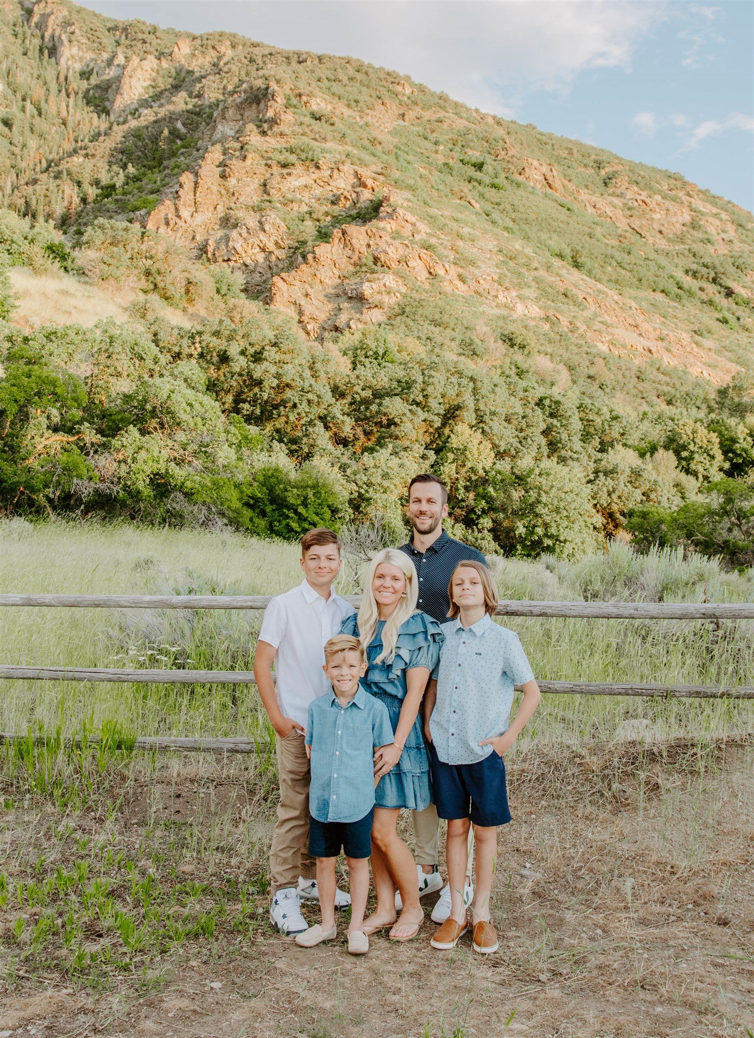 Family group wearing coordinated denim and blue outfits poses together against scenic mountain backdrop.