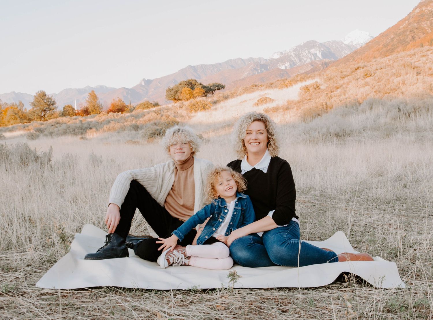 Family group lounging on blanket in golden mountain field during sunset photo session.