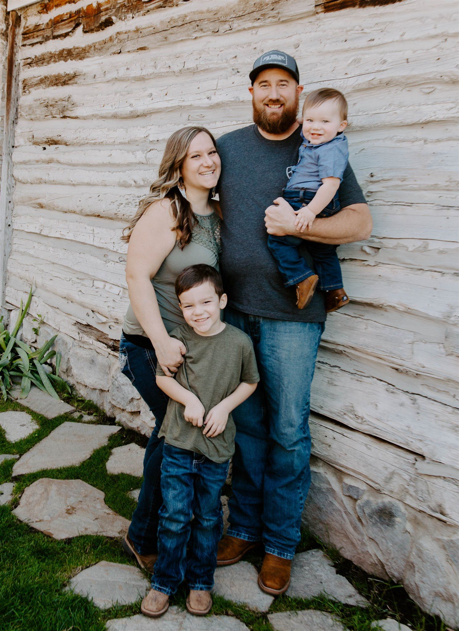 Casual family portrait against weathered wooden wall background in rustic outdoor setting.