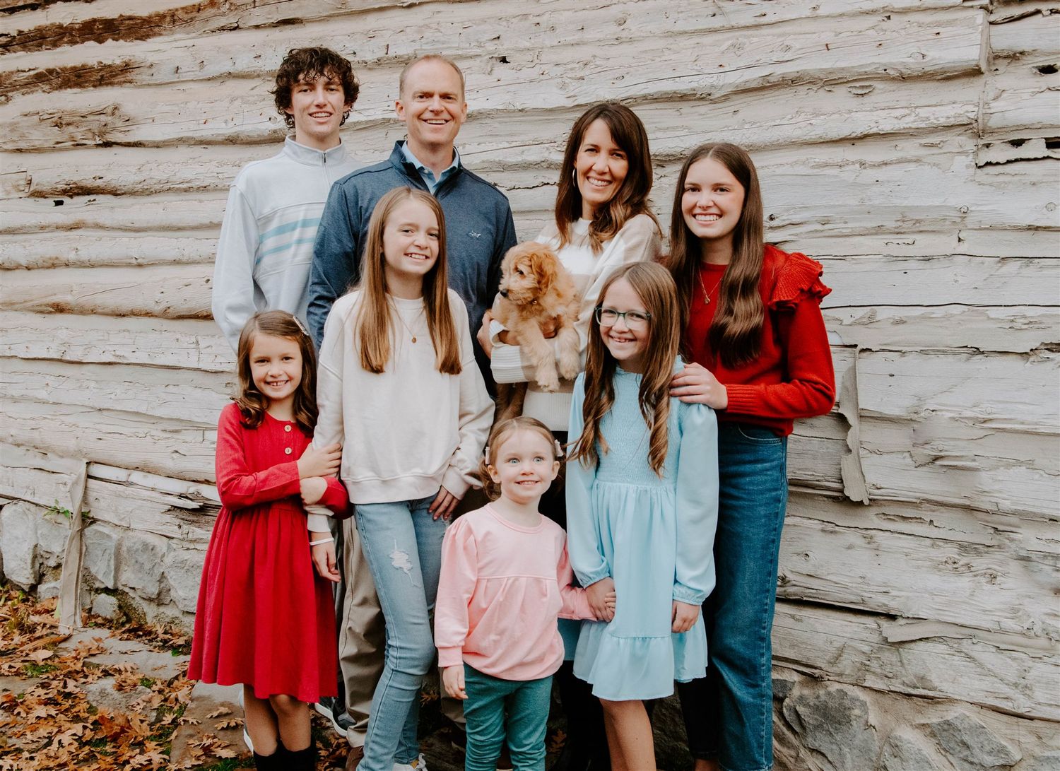 Family portrait against weathered wooden wall with children in coordinated red and casual outfits.