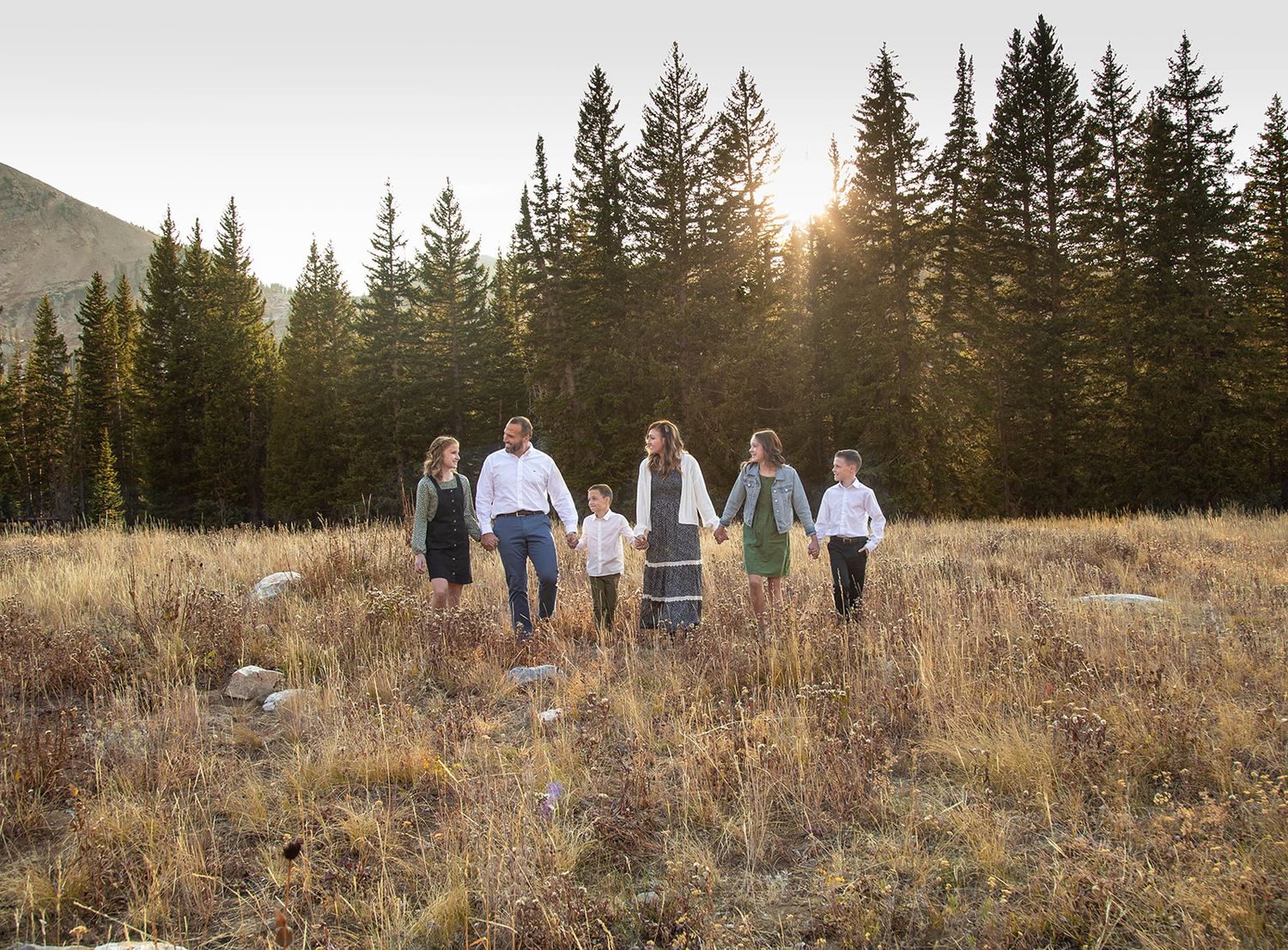A group walking through a mountain meadow at sunset with evergreen trees in the background.