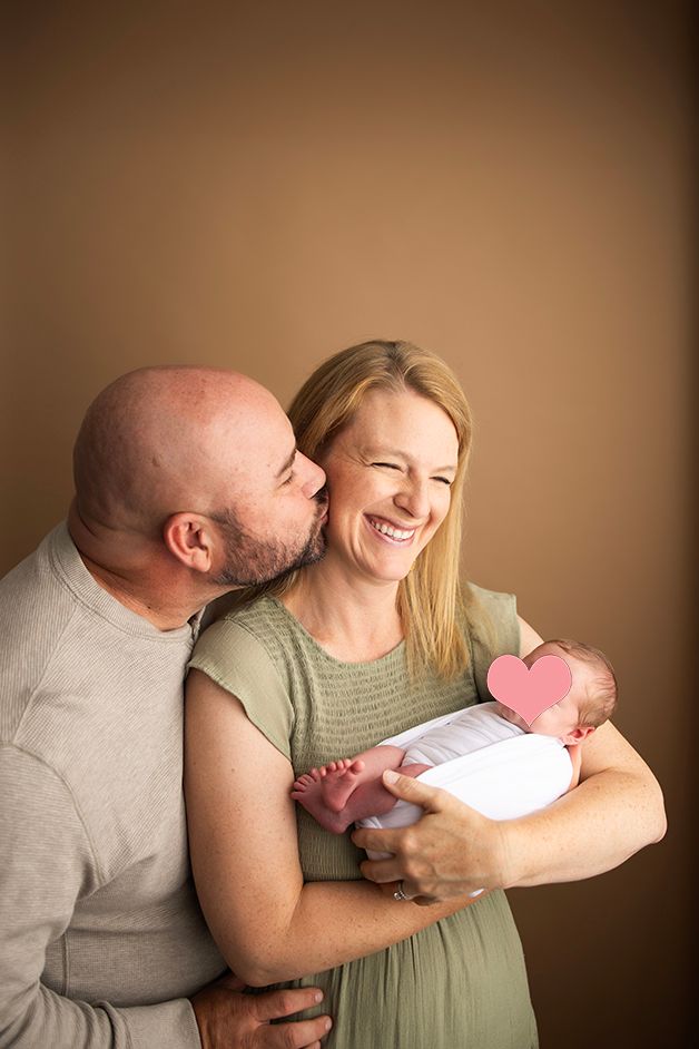 Intimate portrait of couple with newborn baby against warm brown backdrop.