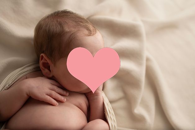 Newborn baby lying on soft cream-colored fabric in artistic portrait style.