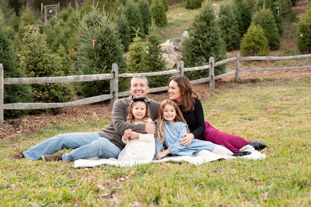 Three people pose together on a grassy hillside under a weeping willow tree.