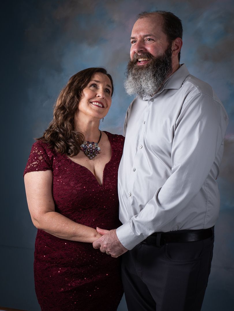 Couple in formal attire sharing an intimate moment against studio backdrop.