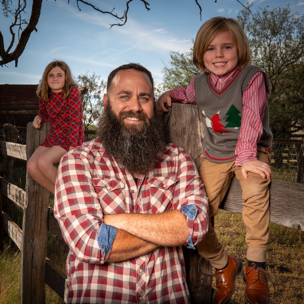 Family members pose on wooden fence outdoors in casual country attire.